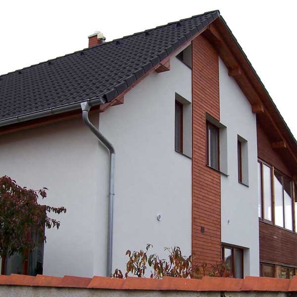 Pohled na bílou fasádu rodinného domu, který obsahuje dřevěnou část